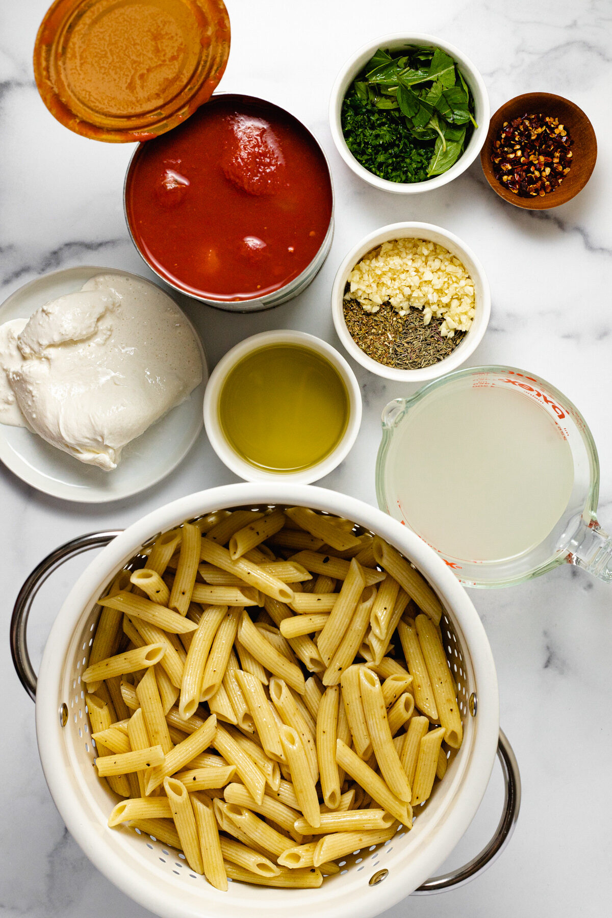White marble counter top with bowls of ingredients to make penne Pomodoro.