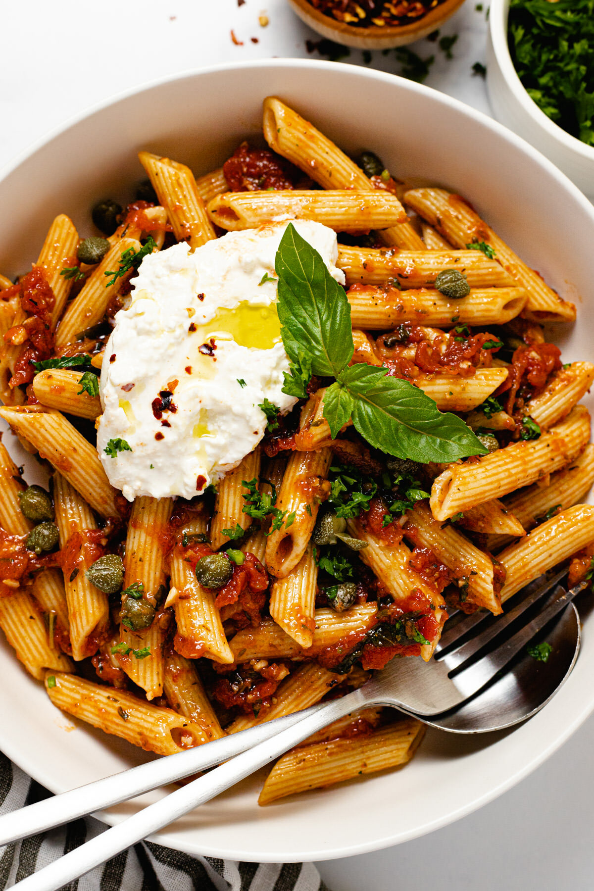 White bowl filled with penne Pomodoro garnished with burrata and basil