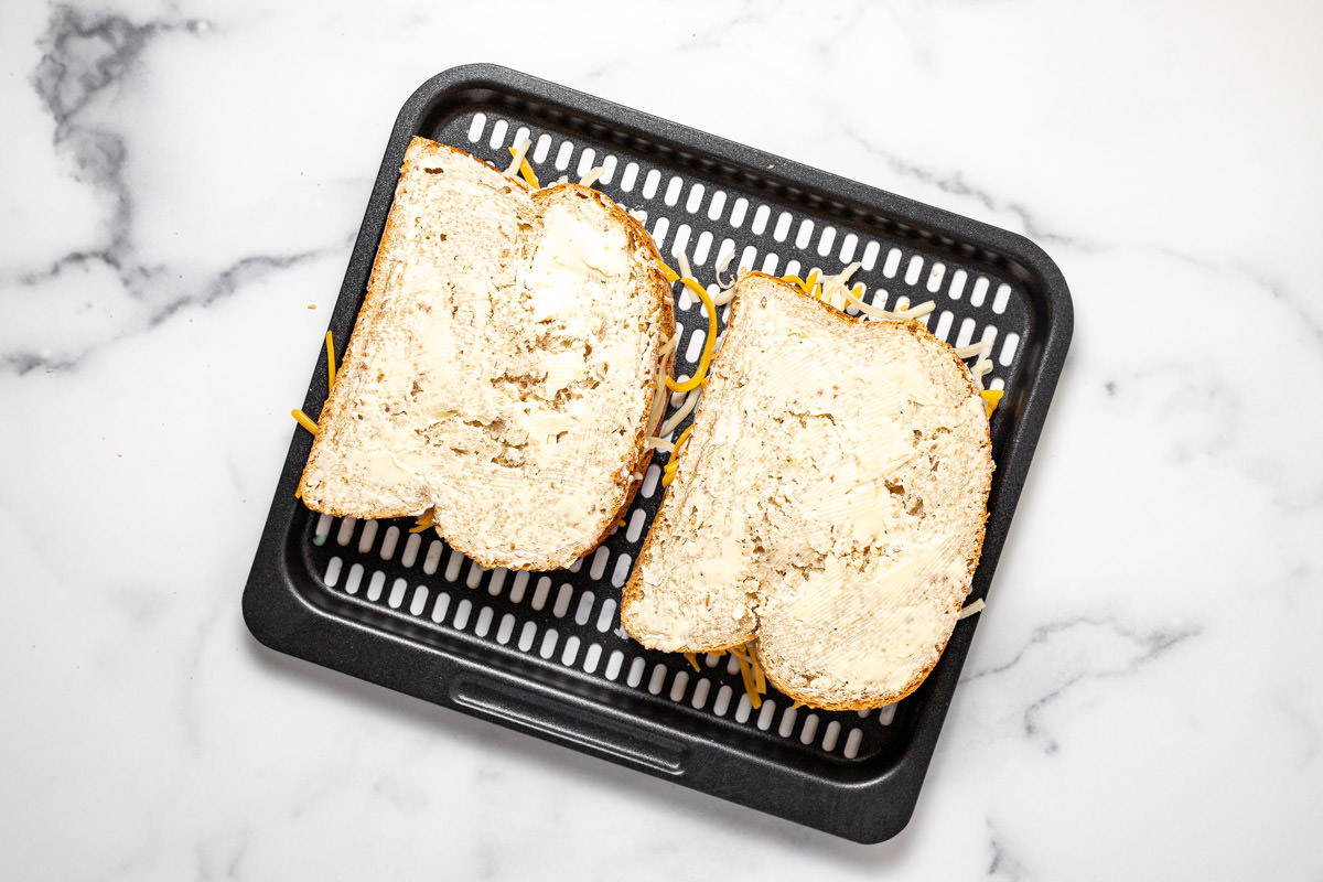 Air fryer tray with two grilled cheese sandwiches ready to go in the oven