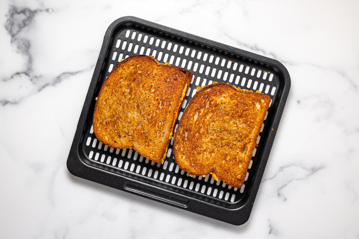 Air fryer tray with two freshly cooked air fryer grilled cheese sandwiches