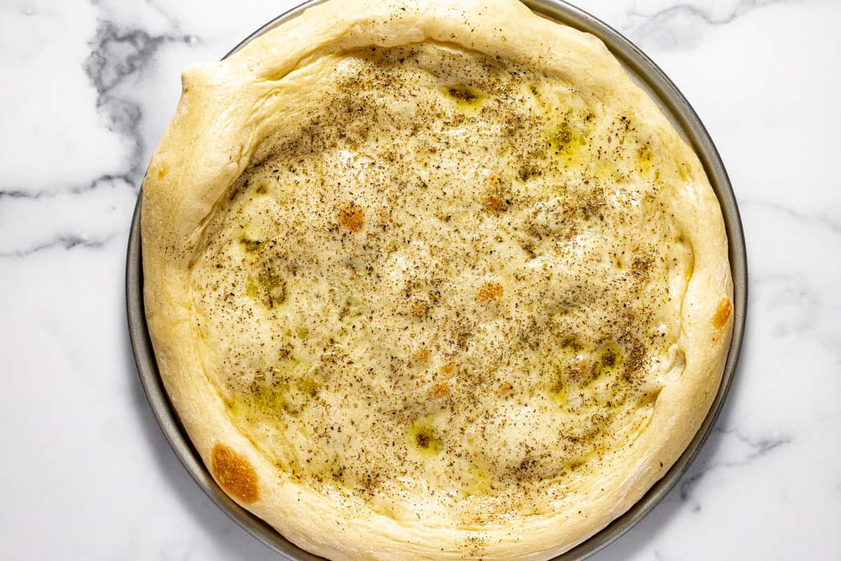 Pizza crust on a pizza pan topped with olive oil an dried oregano