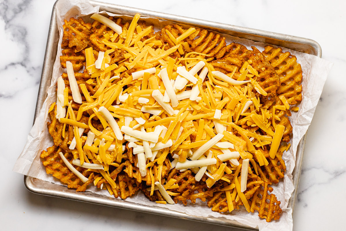 Crispy waffle fries on a parchment lined baking sheet topped with shredded cheese