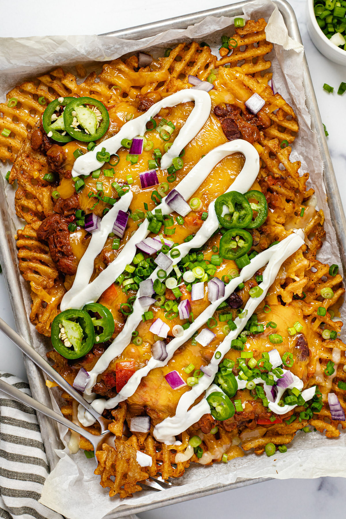 Chili cheese fries on a baking sheet drizzled with sour cream and garnished with green onion