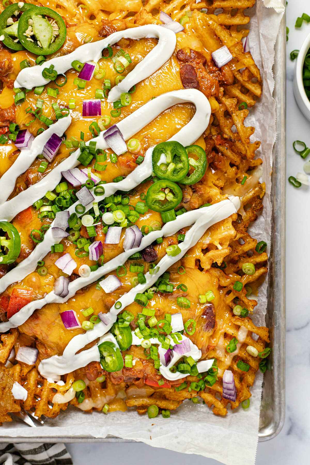 Overhead shot of chili cheese fries on a baking sheet drizzled with sour cream and garnished with green onion