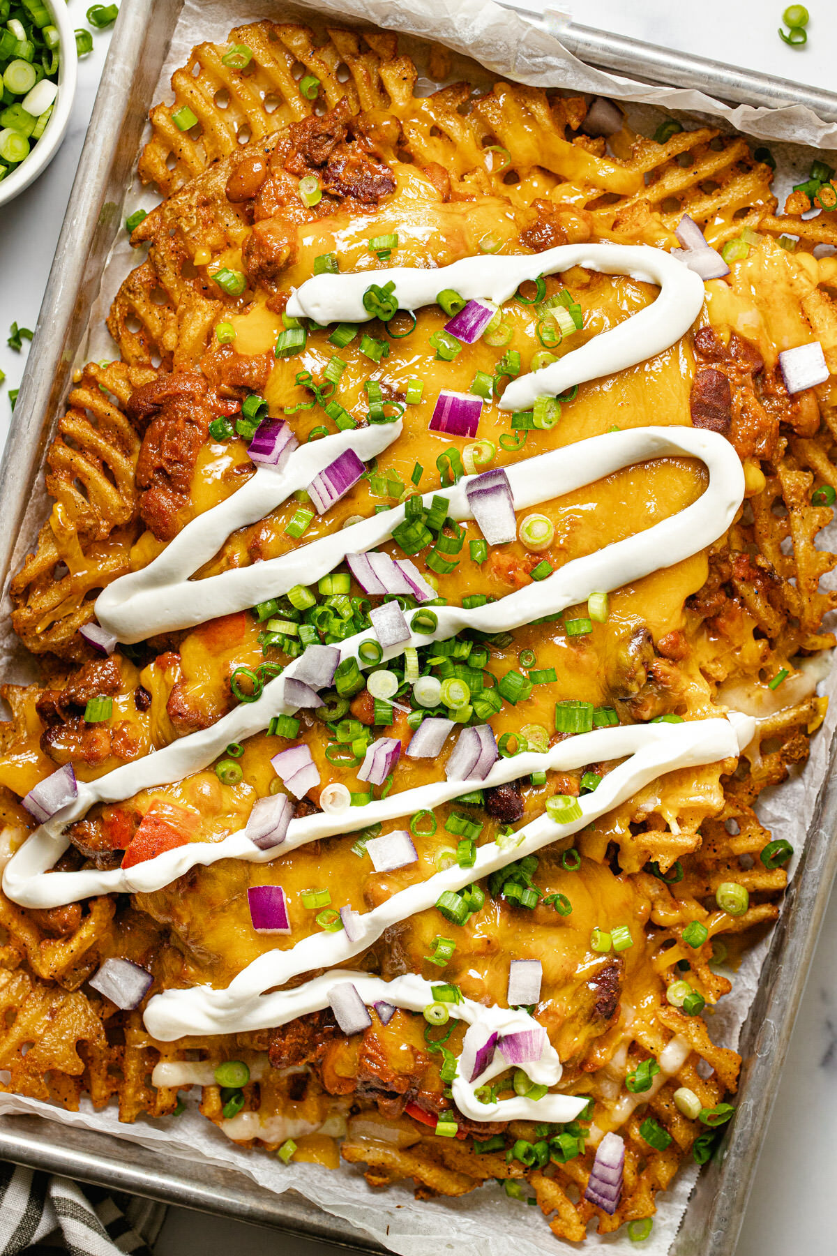 Chili cheese fries on a baking sheet drizzled with sour cream and garnished with green onion