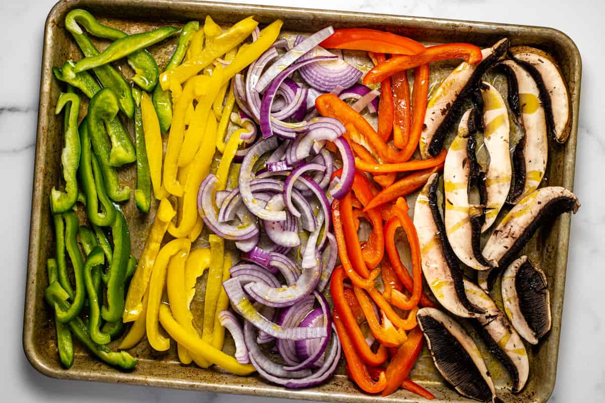 Baking sheet filled with sliced veggies drizzled with olive oil