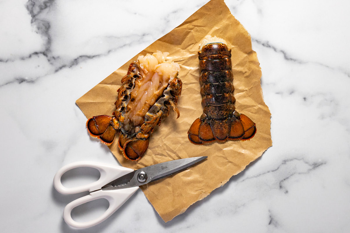 Two lobster tails on butcher paper with a pair of scissors next to them