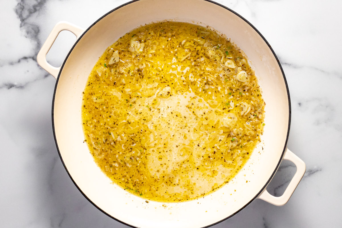 White skillet with olive oil butter garlic herbs and white wine
