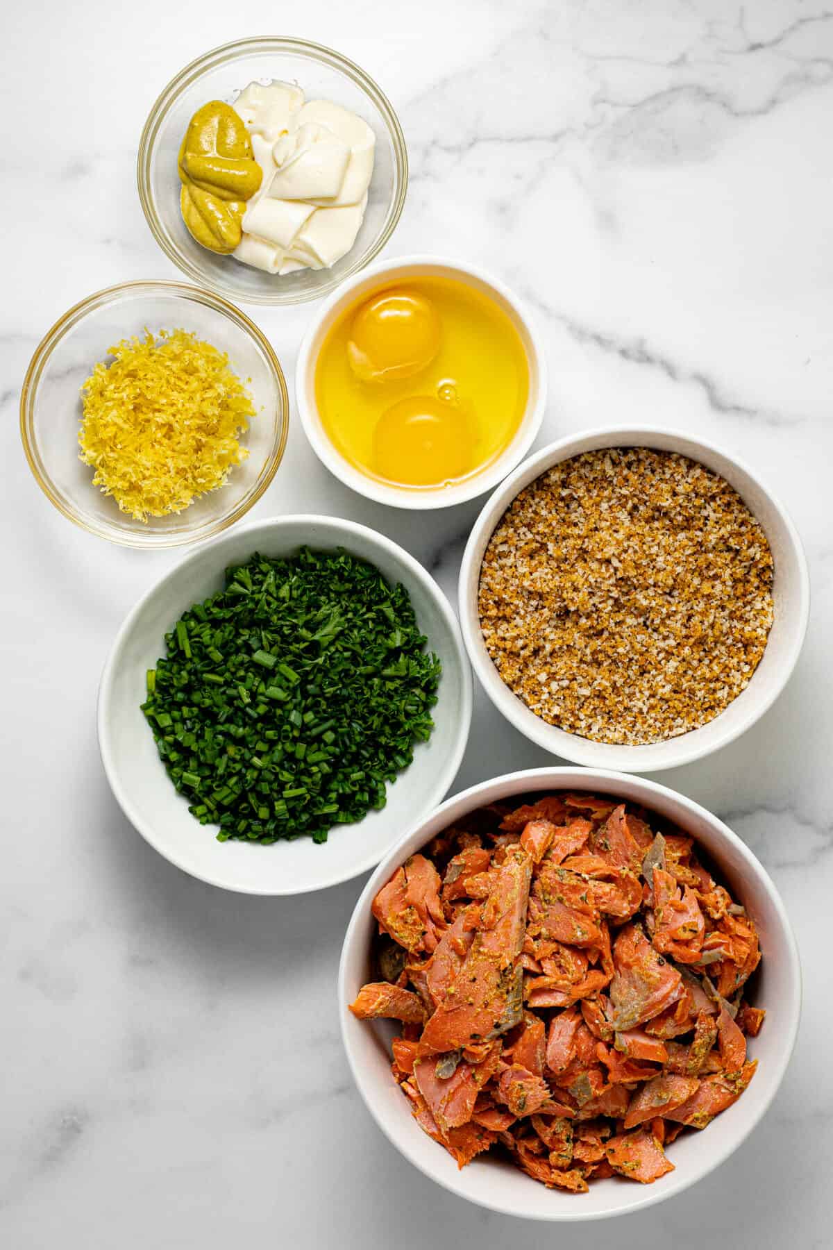White marble counter top with bowls of ingredients to make salmon burgers