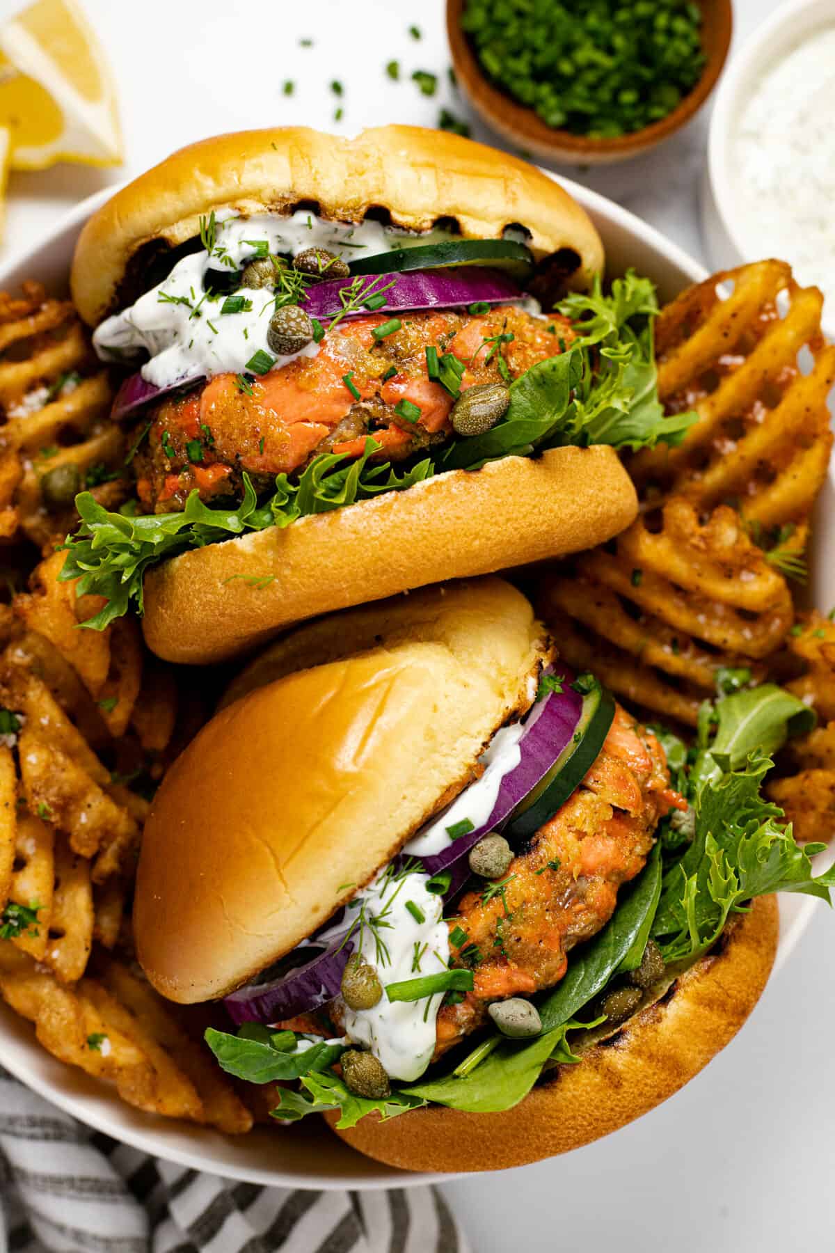 Two salmon burgers in a bowl with waffles fries