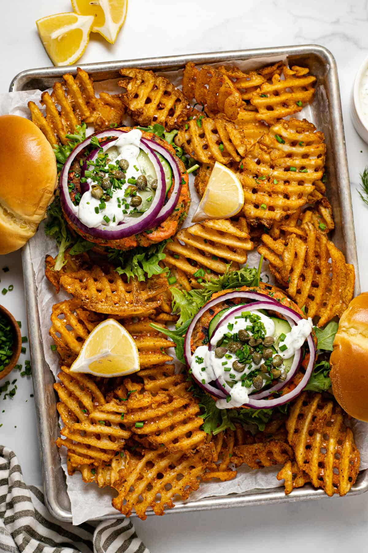 Metal baking sheet with 2 salmon burgers and waffles fries on it