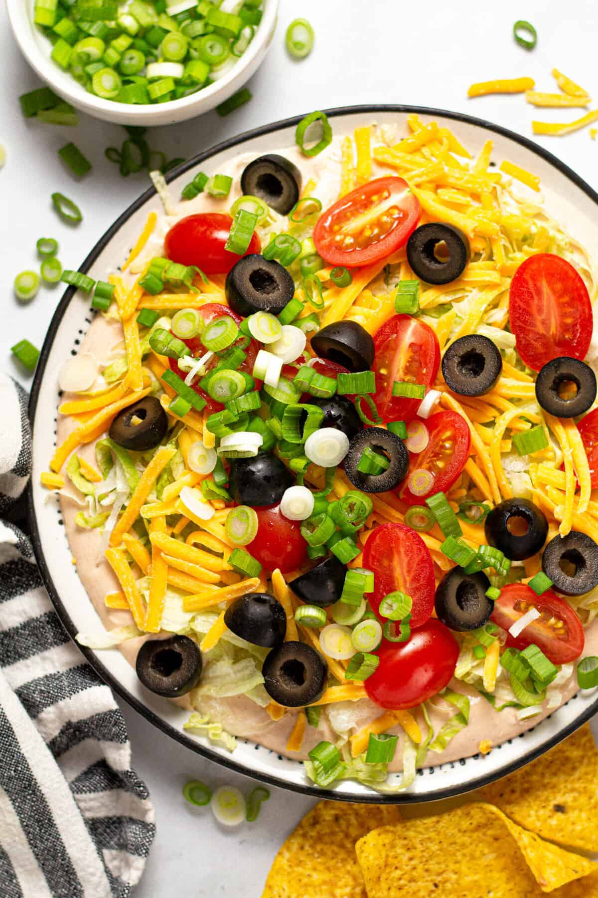 Taco dip on a white plate with tortilla chips around it