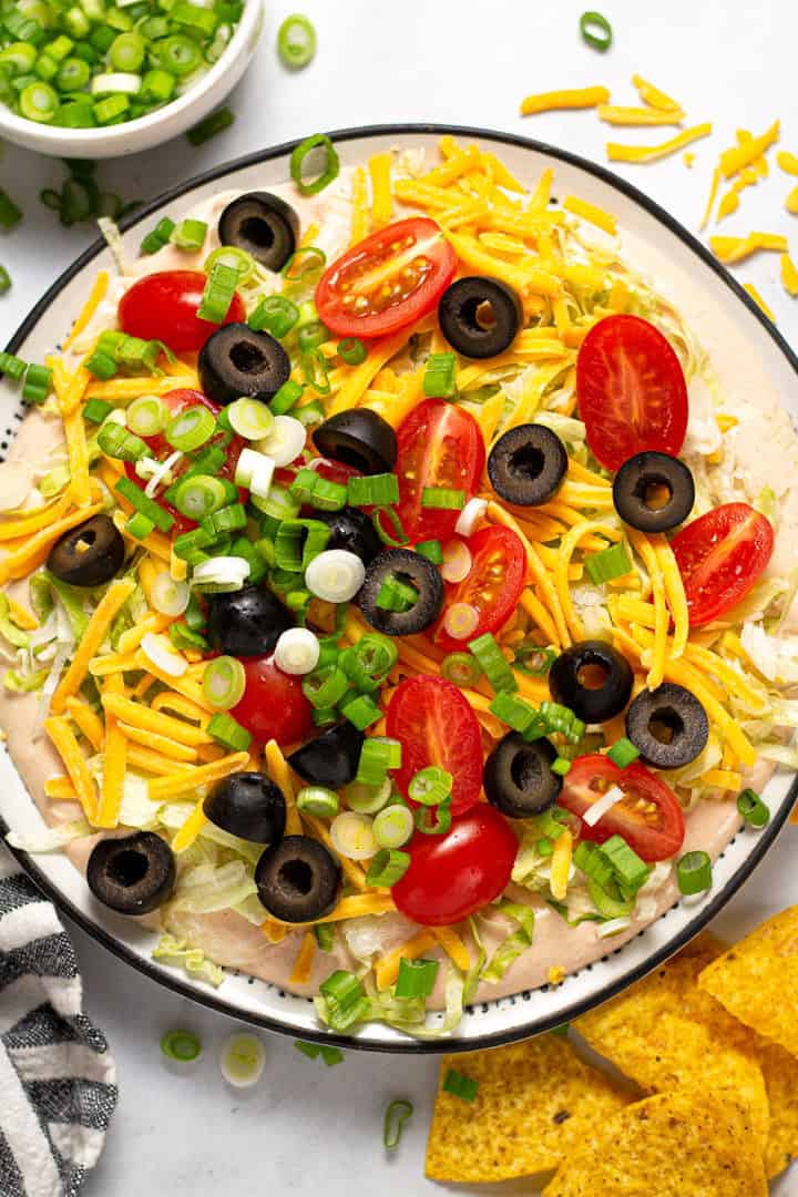 Taco dip on a white plate with tortilla chips around it