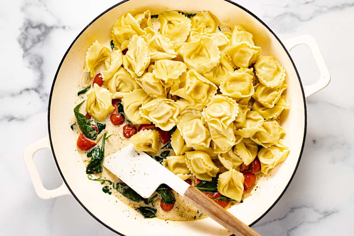Cheese tortellini along with sauce ingredients in a large white pan
