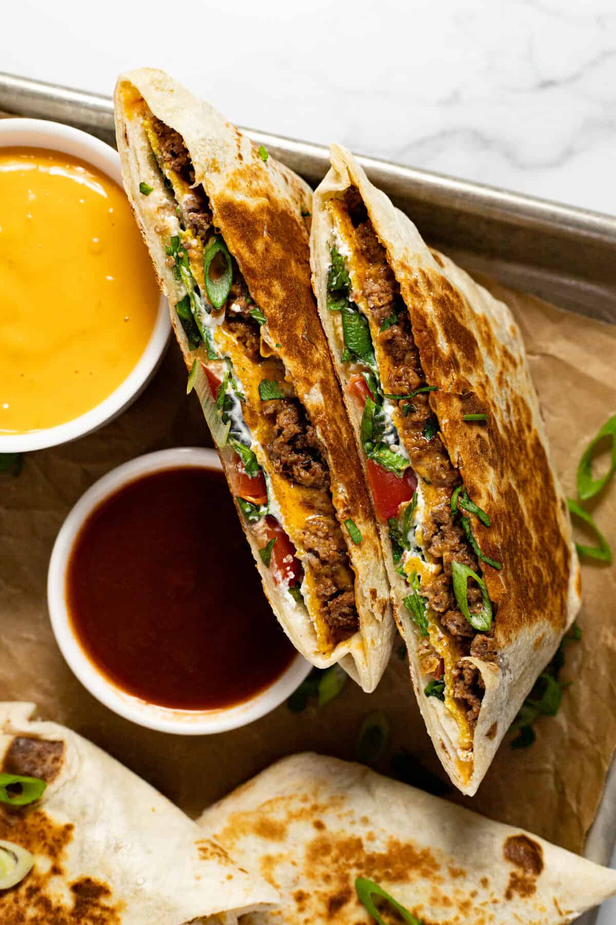 A crunchwrap supreme cut in half on a parchment lined baking sheet