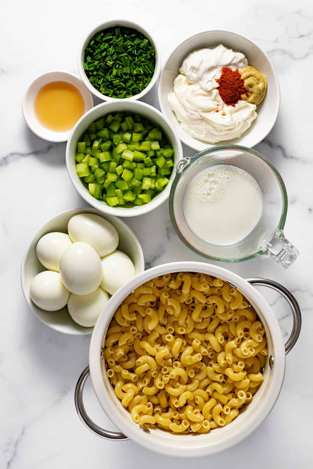 White marble counter top with bowls of ingredients to make deviled egg pasta salad