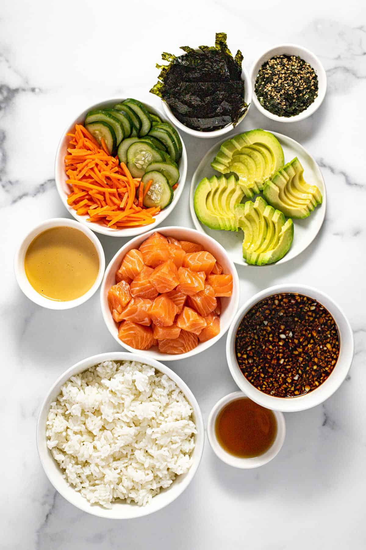 White marble countertop with bowls of ingredients to make a salmon sushi bowl