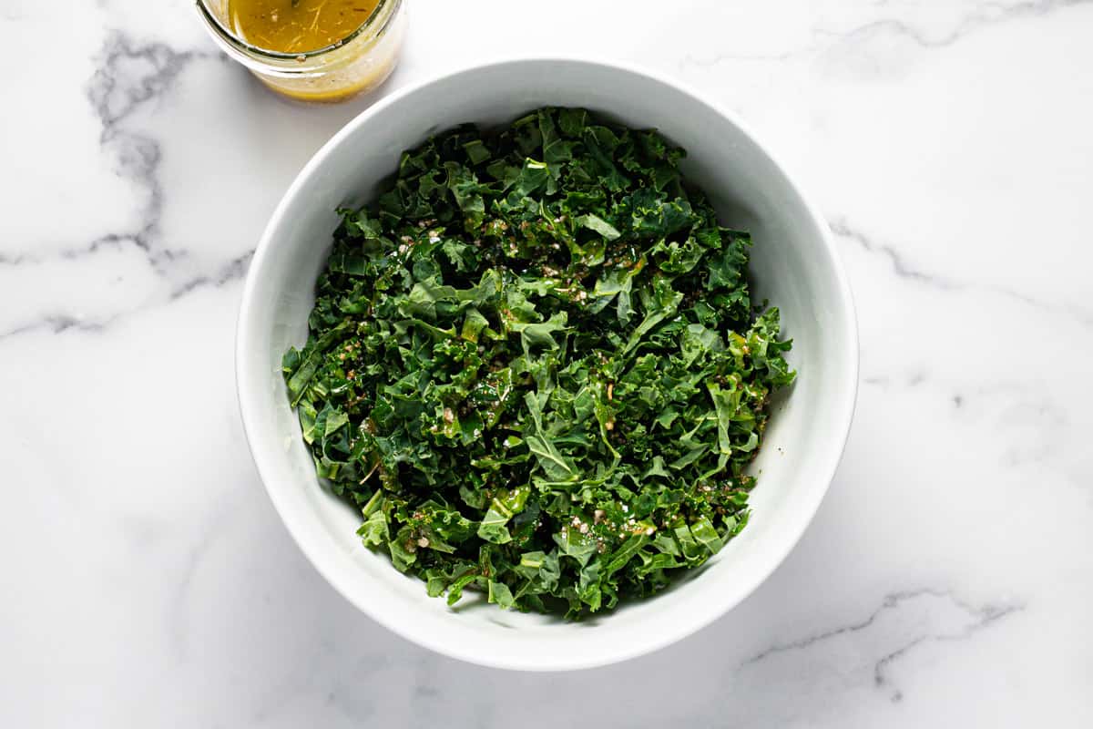 White bowl filled with kale with dressing poured over it