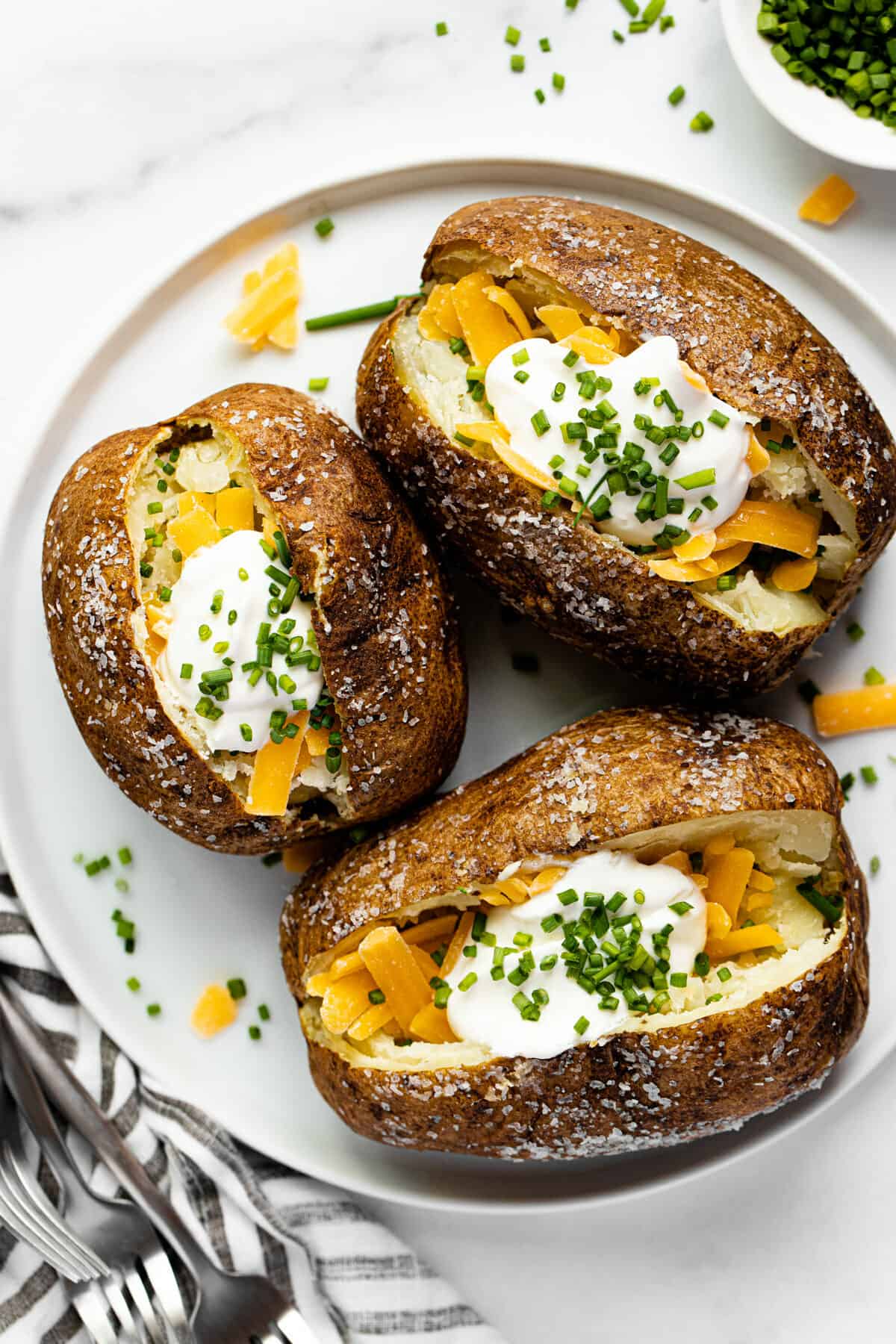 White dish stuffed with baked potatoes in an air fryer topped with cheese and sour cream