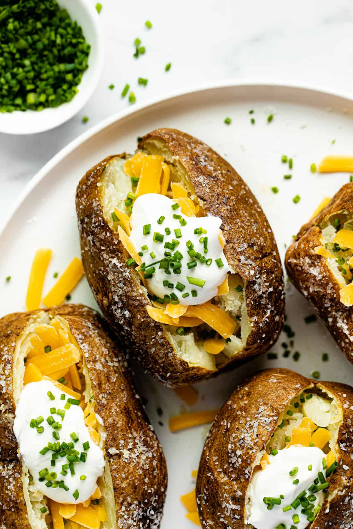 White dish stuffed with baked potatoes in an air fryer topped with cheese and sour cream