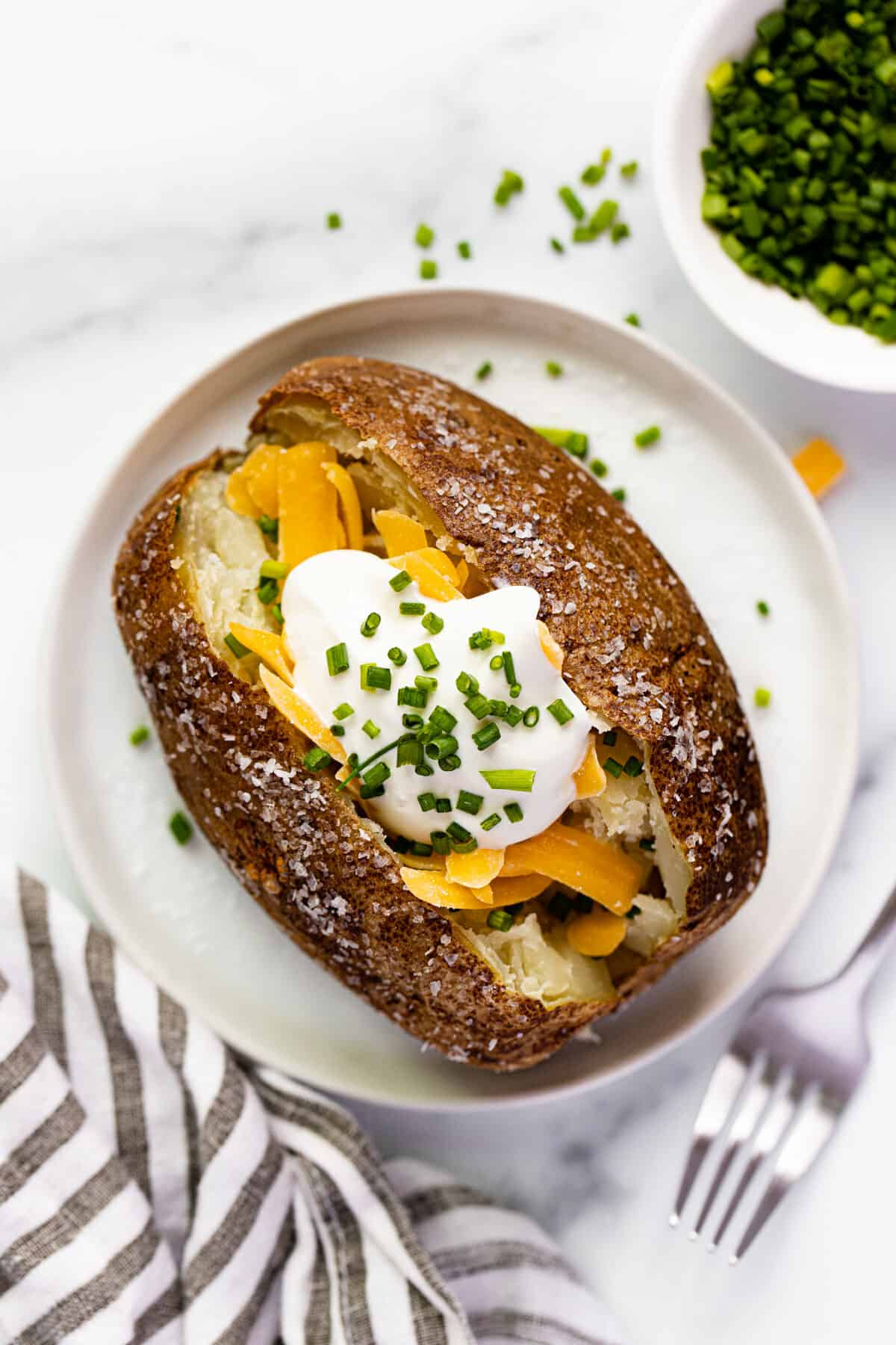 Small white plate with air fryer baked potato topped with cheese and sour cream