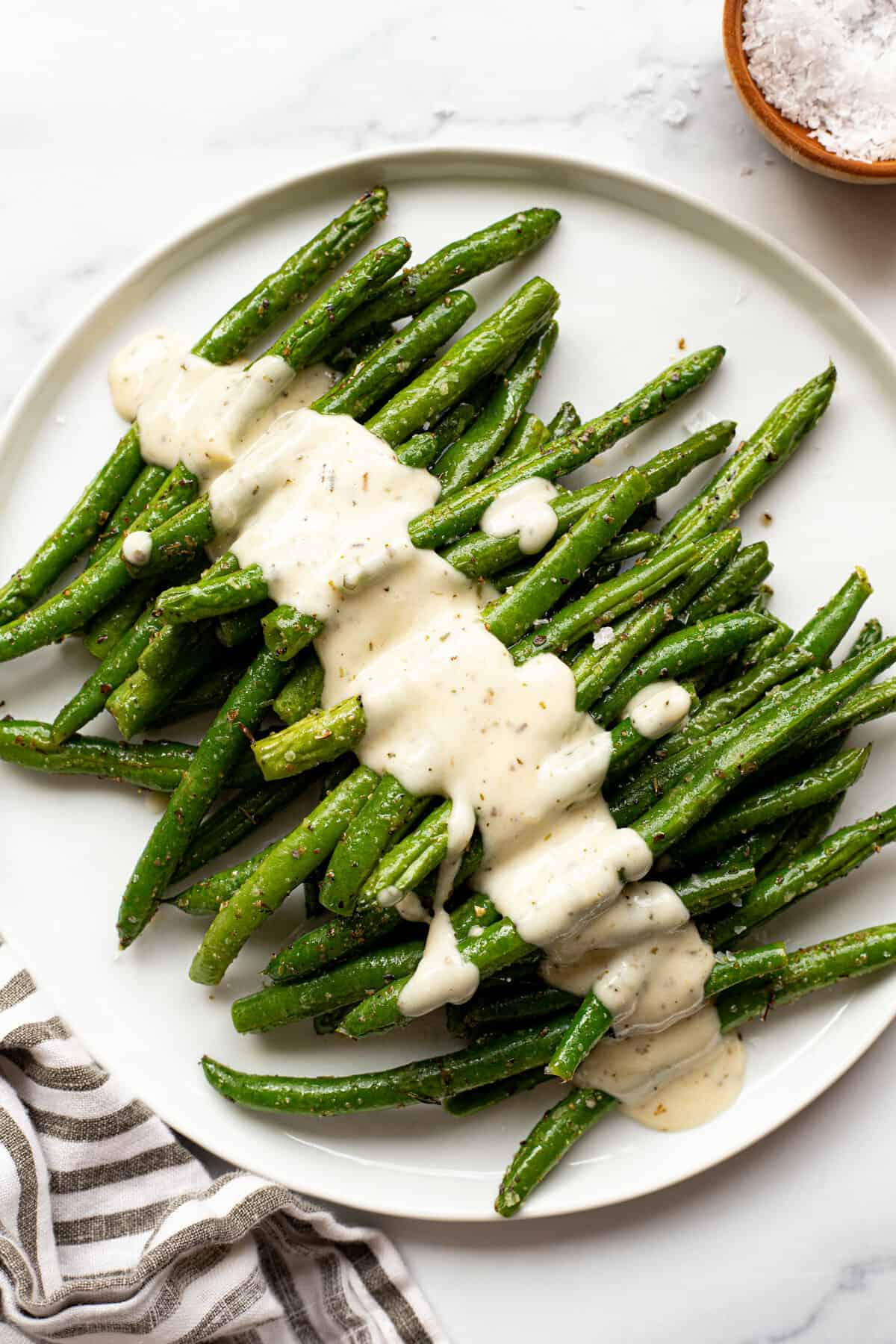 White plate filled with air fryer green beans drizzled with garlic Parmesan sauce