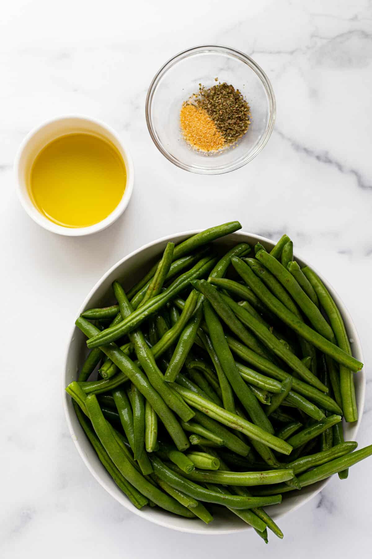 White marble counter top with bowls of ingredients to make air fryer green beans