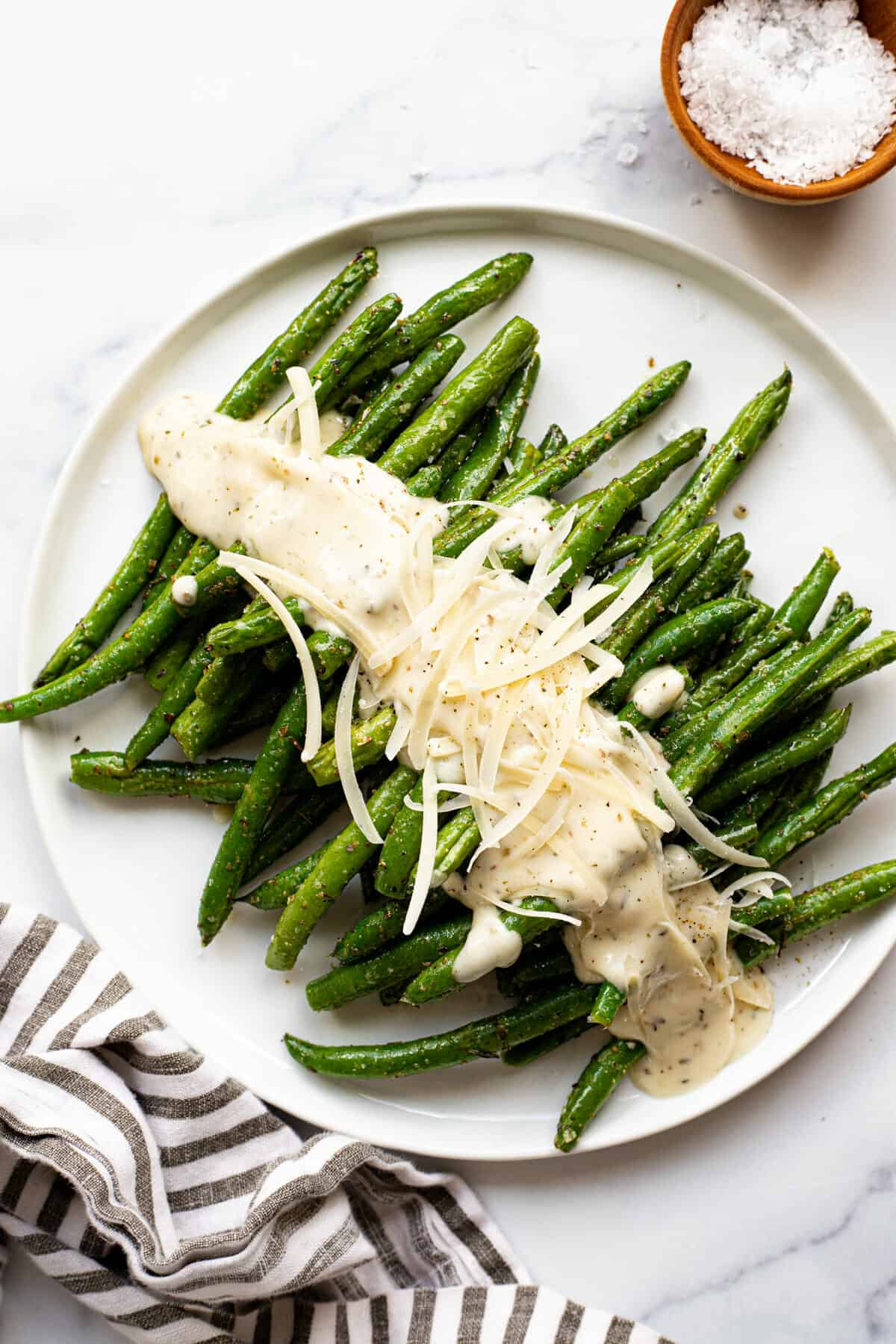 White plate filled with air fryer green beans drizzled with garlic Parmesan sauce