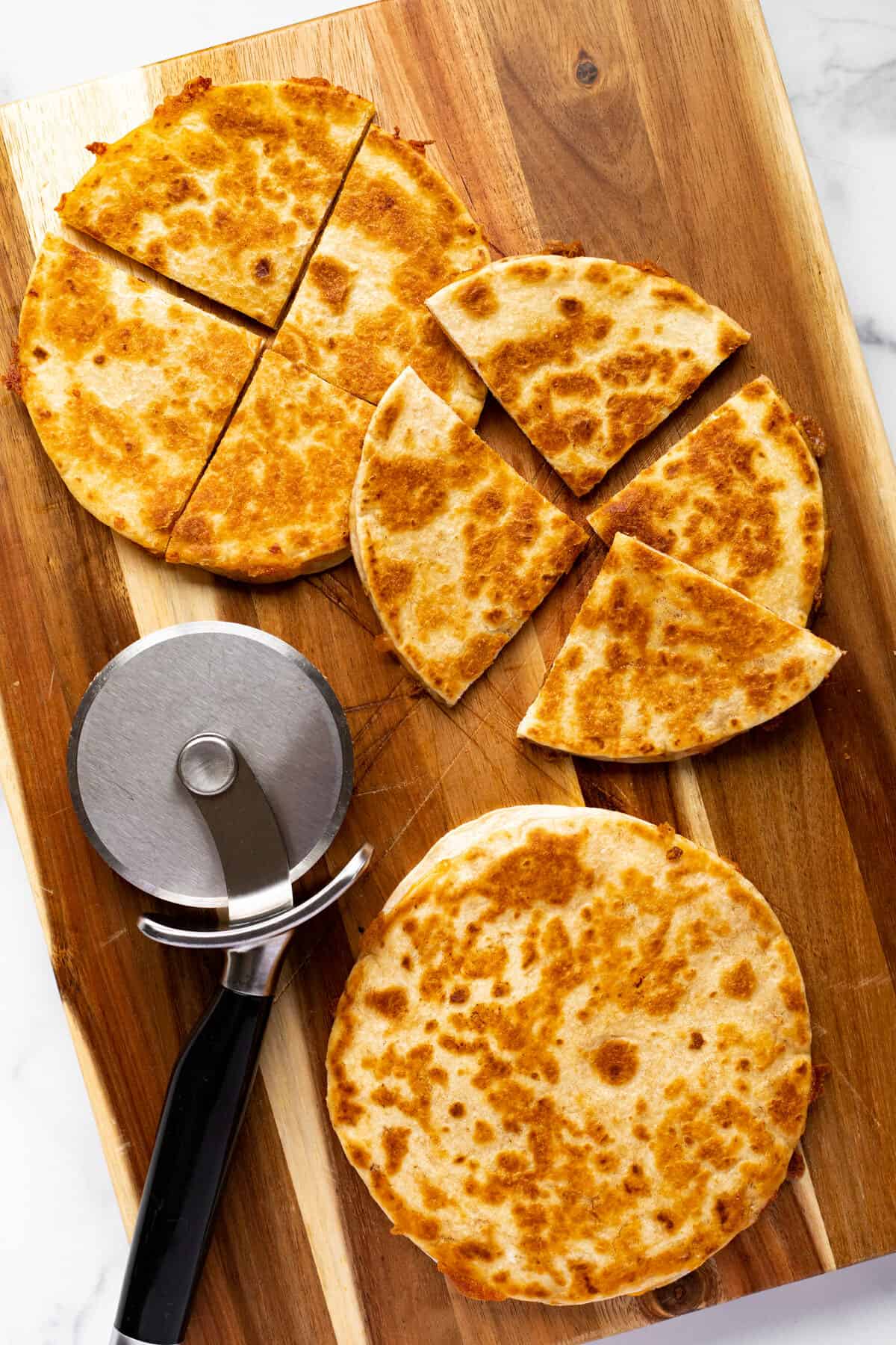 Wooden cutting board with three homemade cheese quesadillas