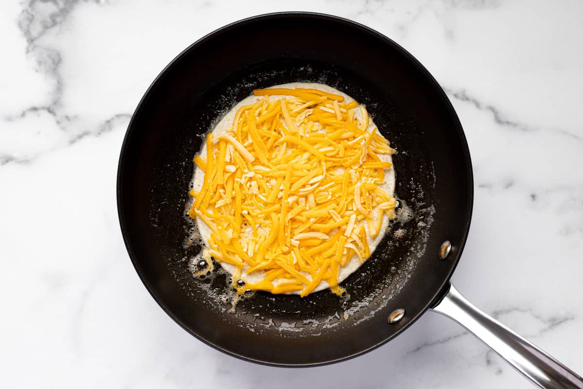 Black skillet with a tortilla covered with shredded cheese