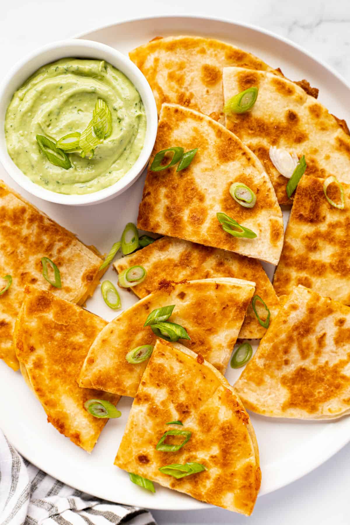 White plate with homemade cheese quesadillas garnished with sliced green onion