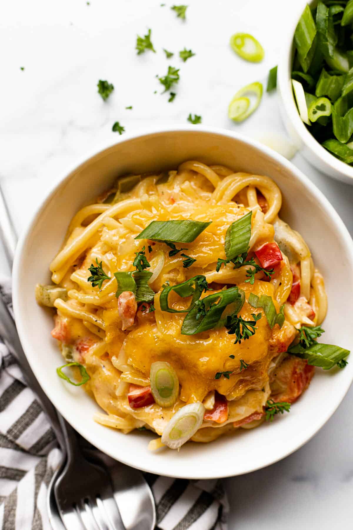 White bowl filled with cheesy chicken spaghetti garnished with green onion