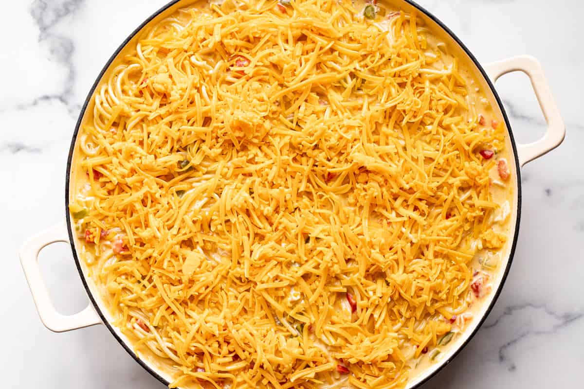 Homemade chicken spaghetti casserole in a large white pan topped with cheddar cheese