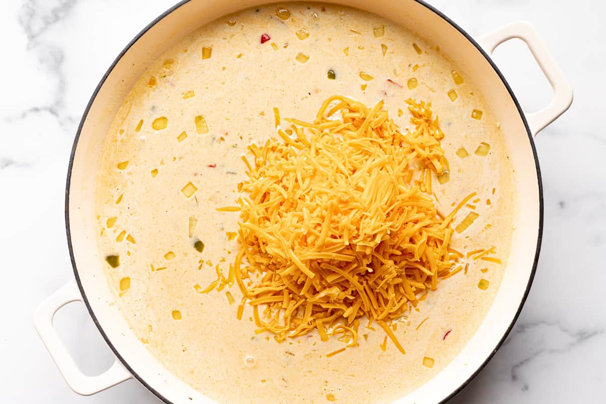 Shredded cheddar cheese being added to a cream sauce