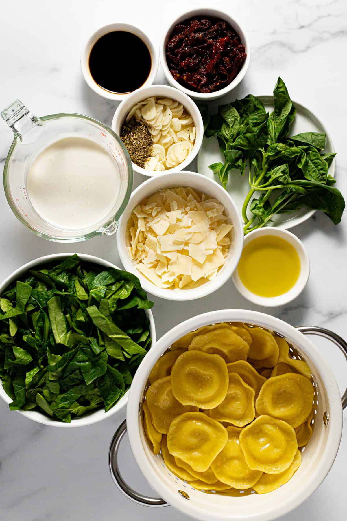 White marble counter top with bowls of ingredients to make creamy ravioli sauce