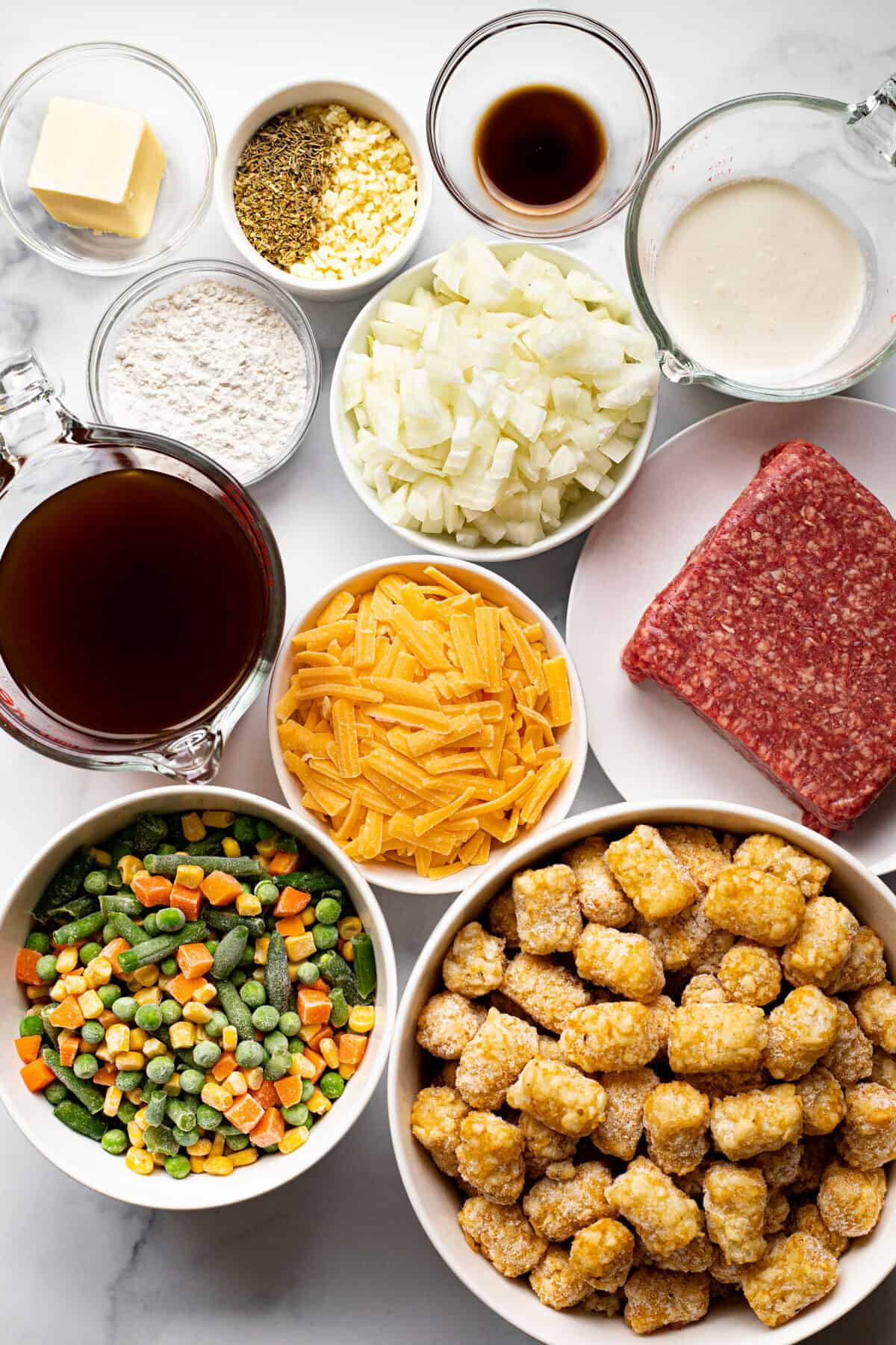 White marble counter top with bowls of ingredients to make tater tot hotdish
