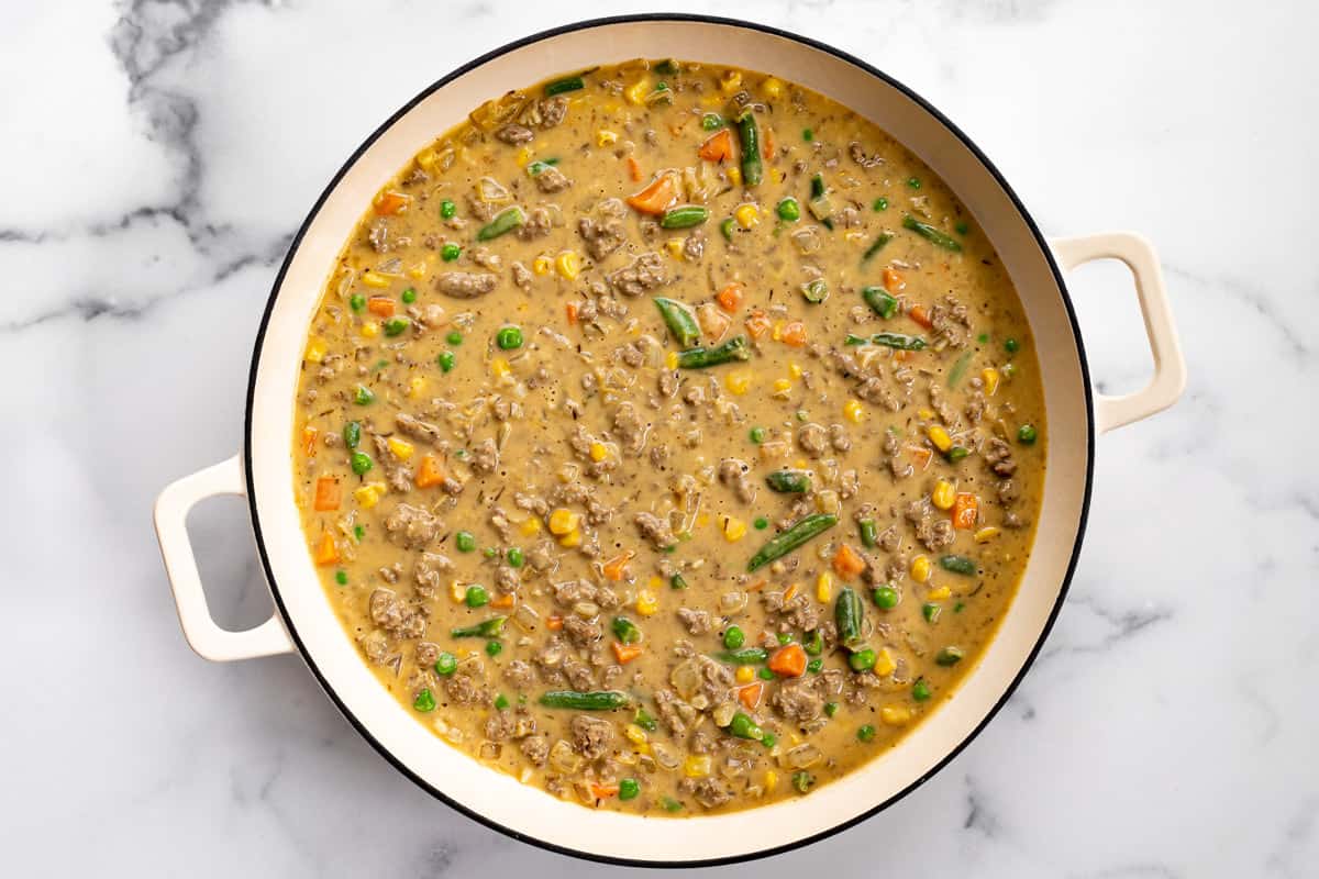 Large white pan filled with gravy ground beef and frozen veggies