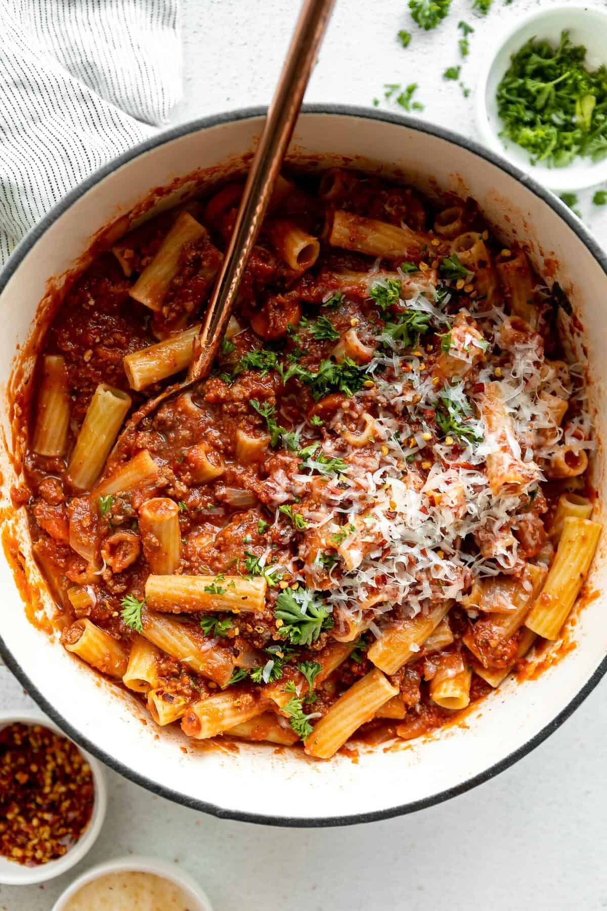 A large pot of homemade rigatoni bolognese garnished with Parmesan and parsley.