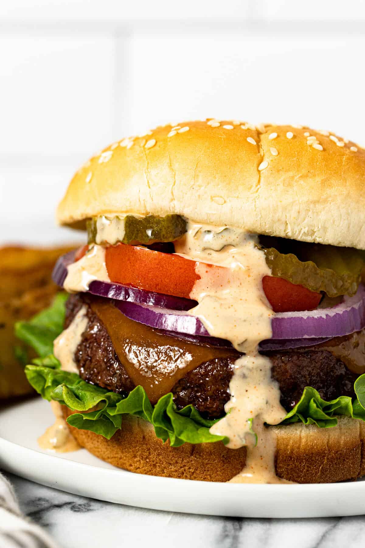 Close up shot of a burger on a white plate drizzled with creamy burger sauce.