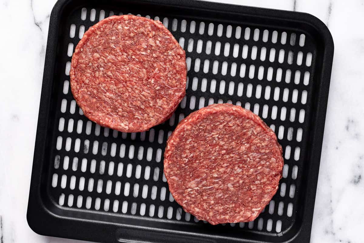 Air fryer tray with two raw hamburgers on it.