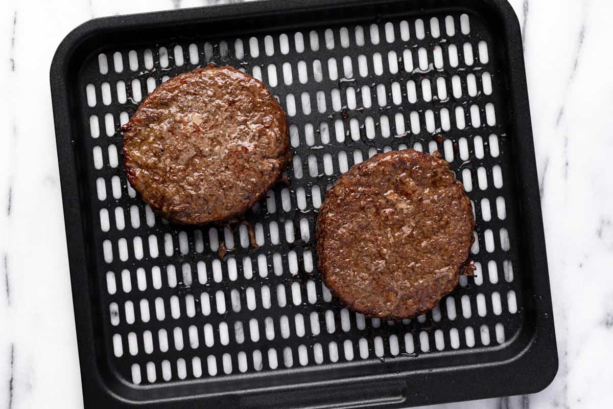 Air fryer tray with cooked hamburgers on it.