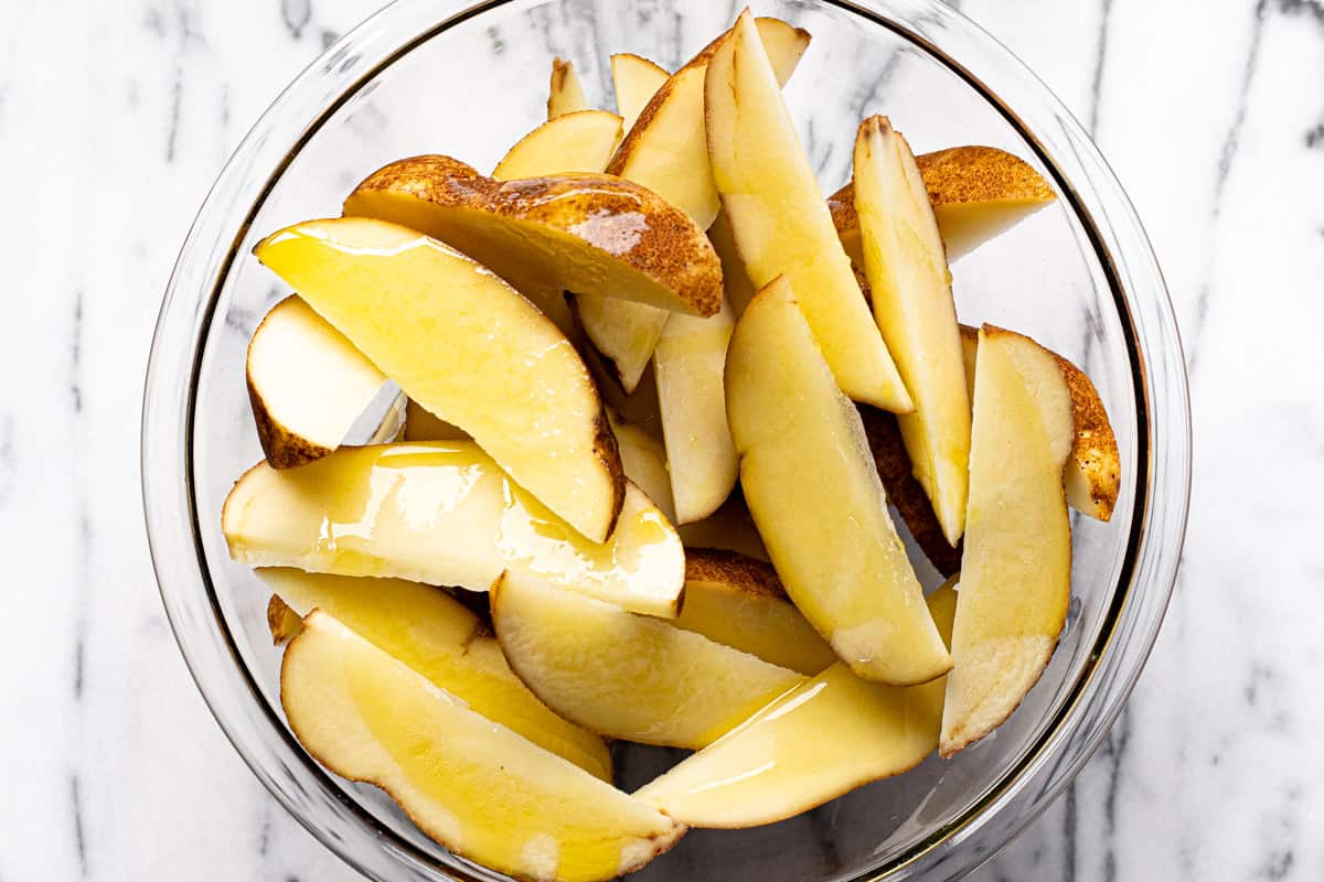 Glass bowl filled with potato wedges drizzled with olive oil.