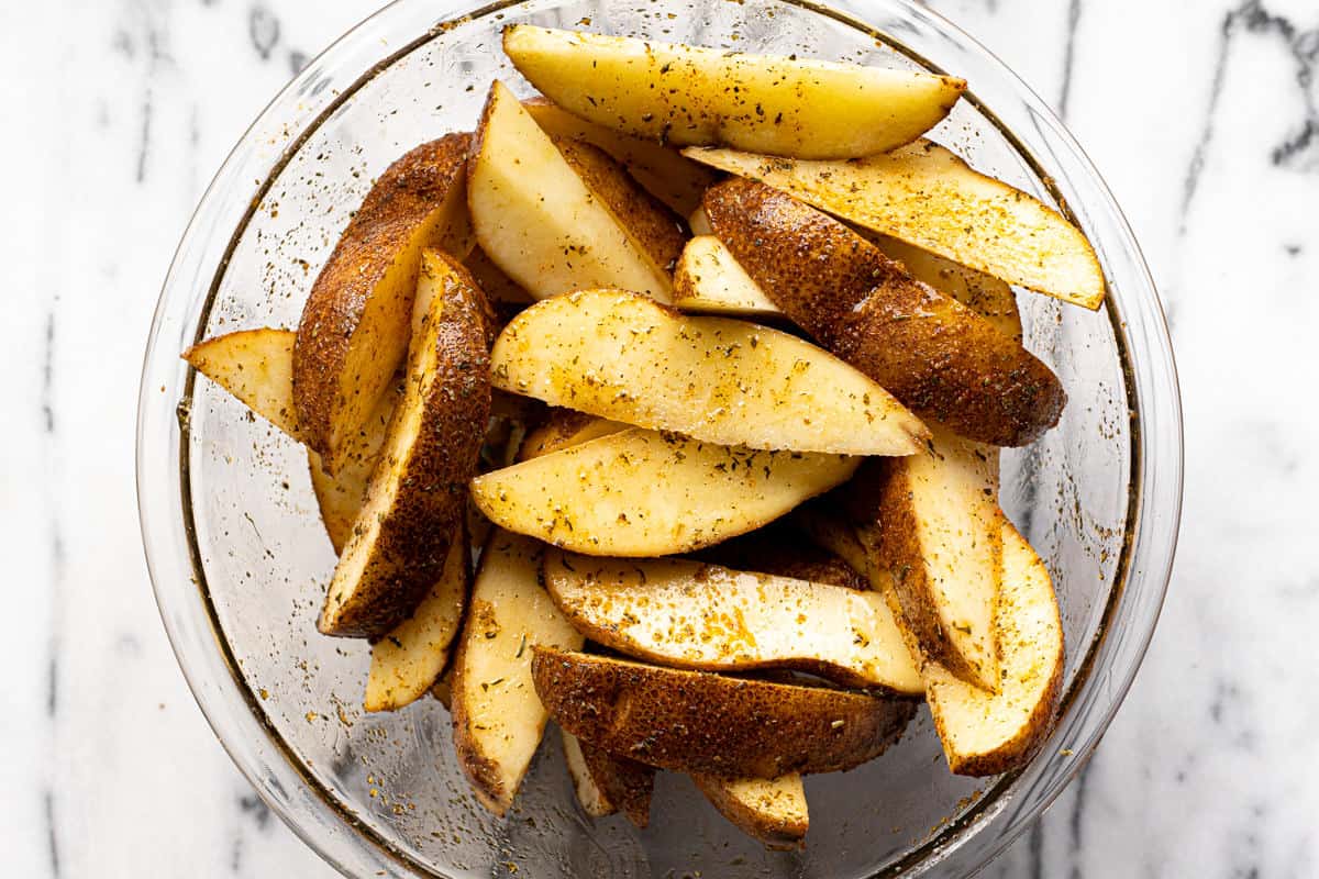 Glass bowl filled with herb seasoned potato wedges.