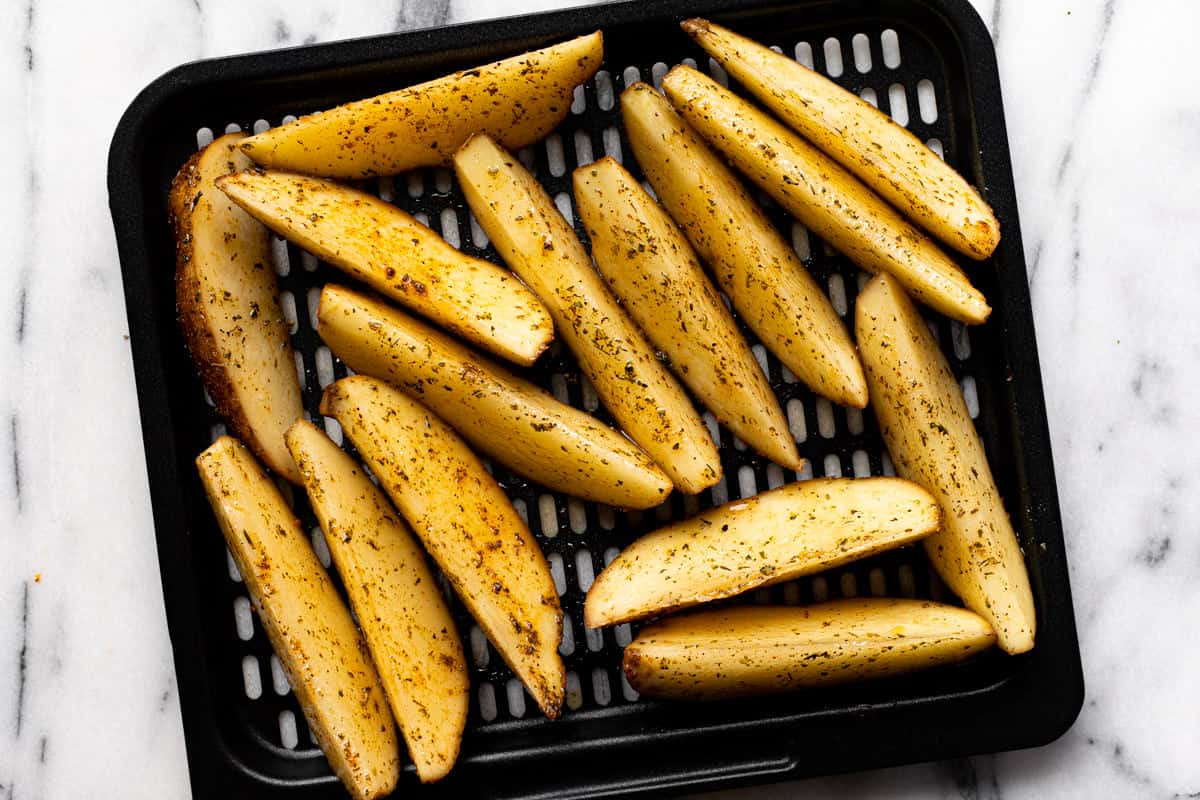 Seasoned potato wedges on an air fryer tray.