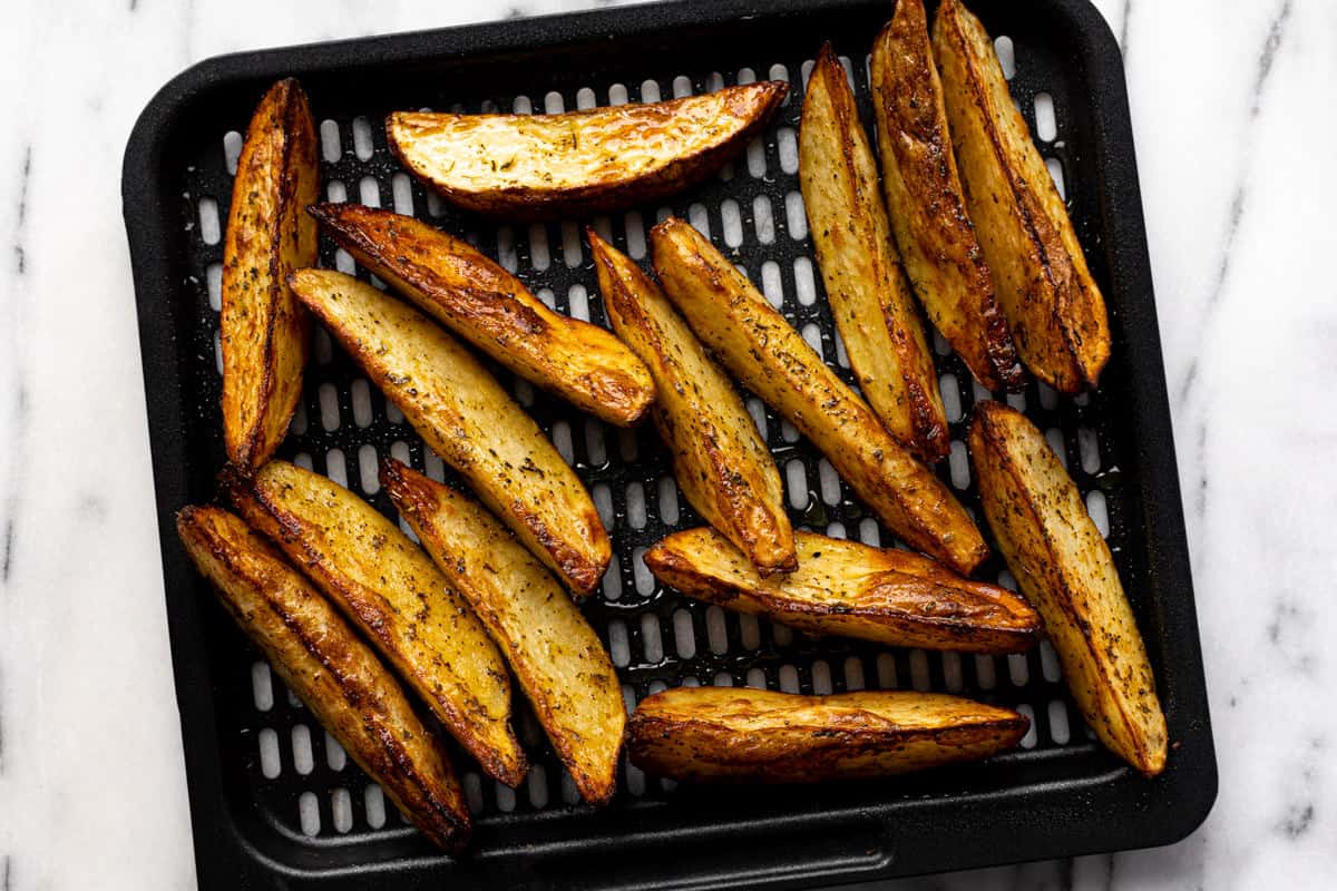 Freshly baked air fryer potato wedges on an air fryer tray.