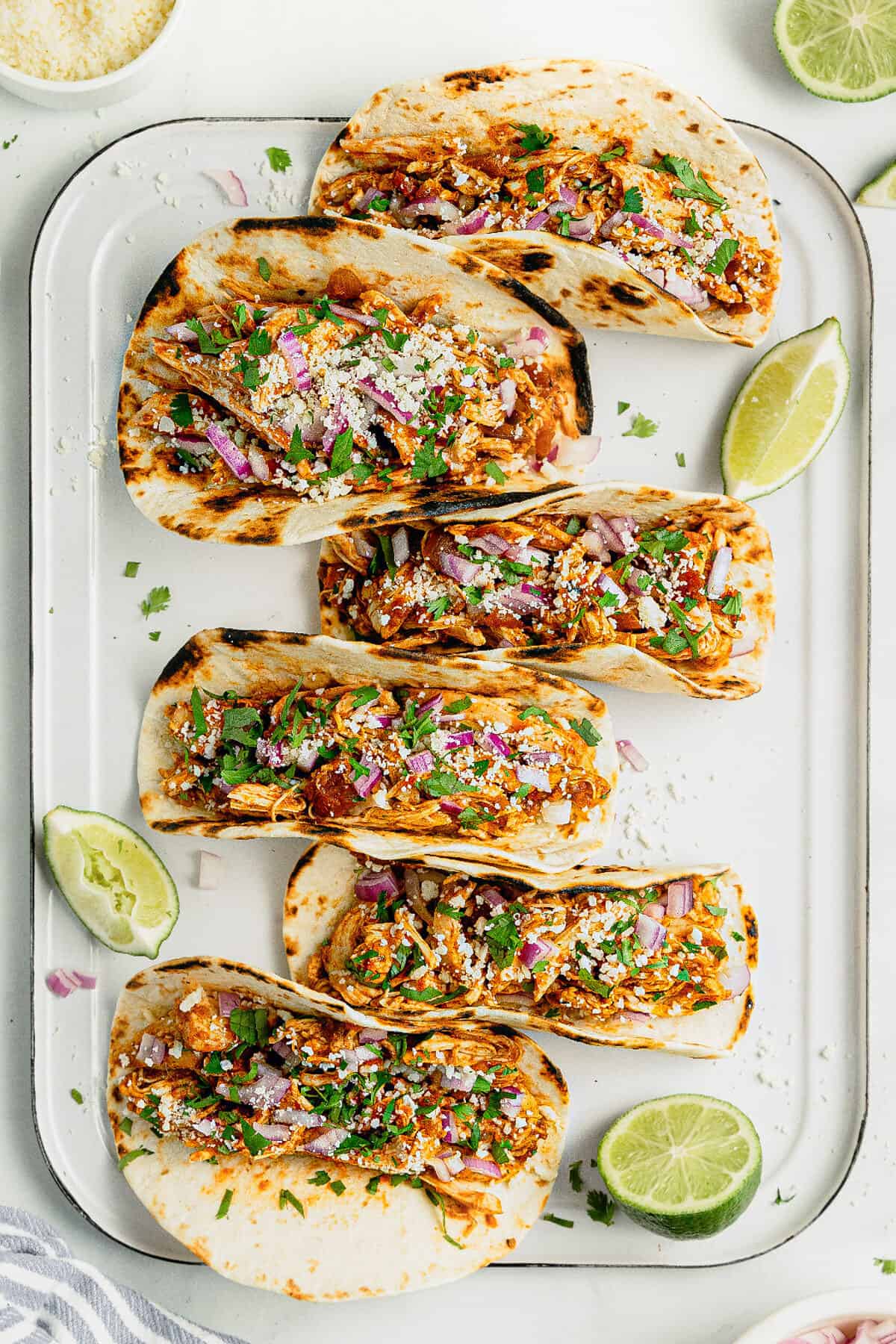White tray filled with chicken tacos topped with onion and Cotija cheese.