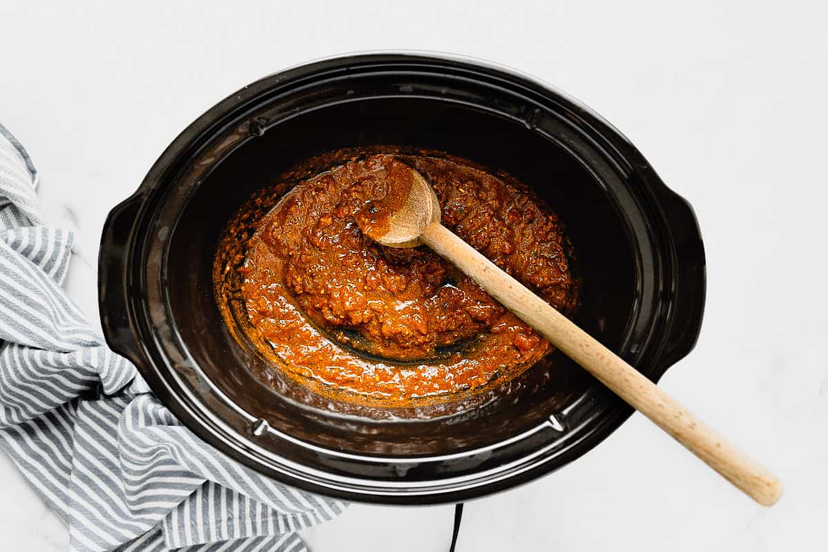 Black crock pot insert with salsa mixed with taco seasoning.