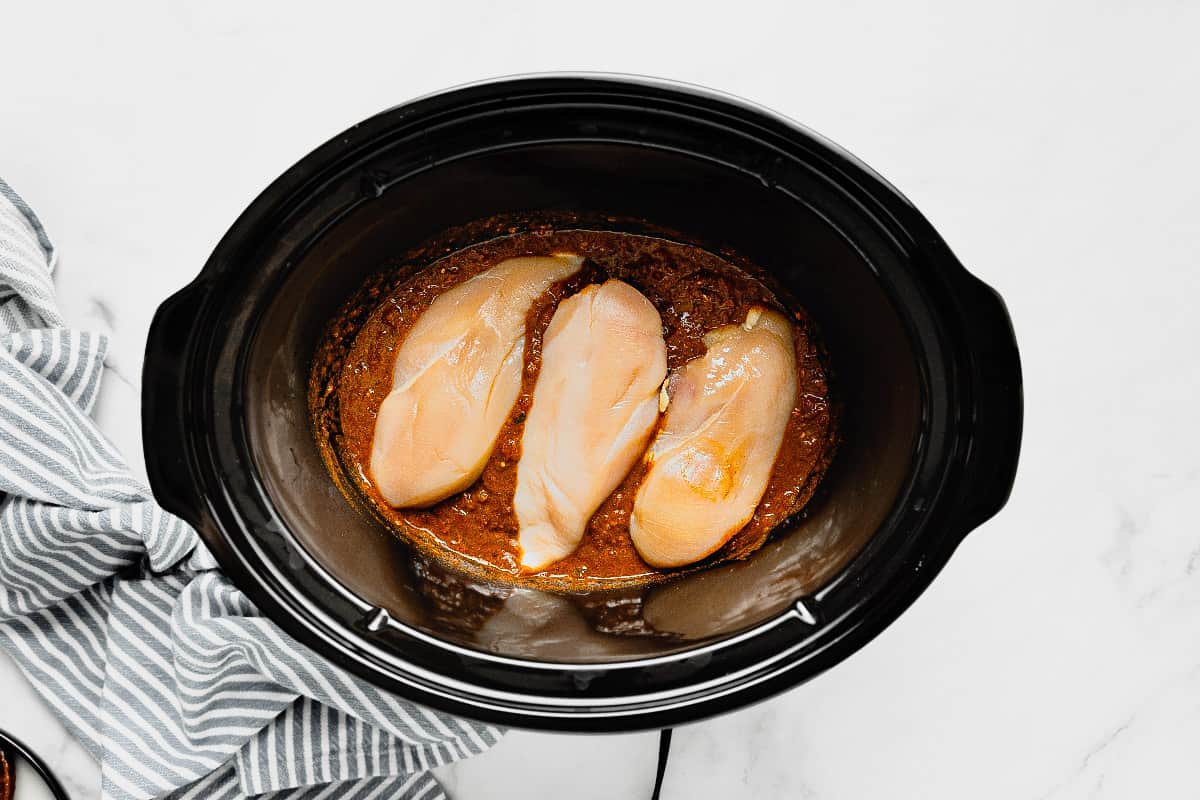 Black crock pot insert with salsa and chicken breast in it.