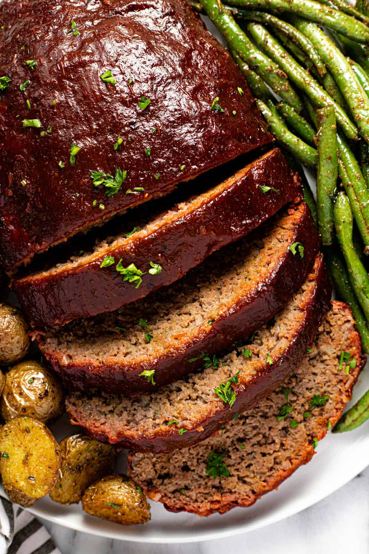 Close up shot of sliced smoked meatloaf on a plate with potatoes and green beans.