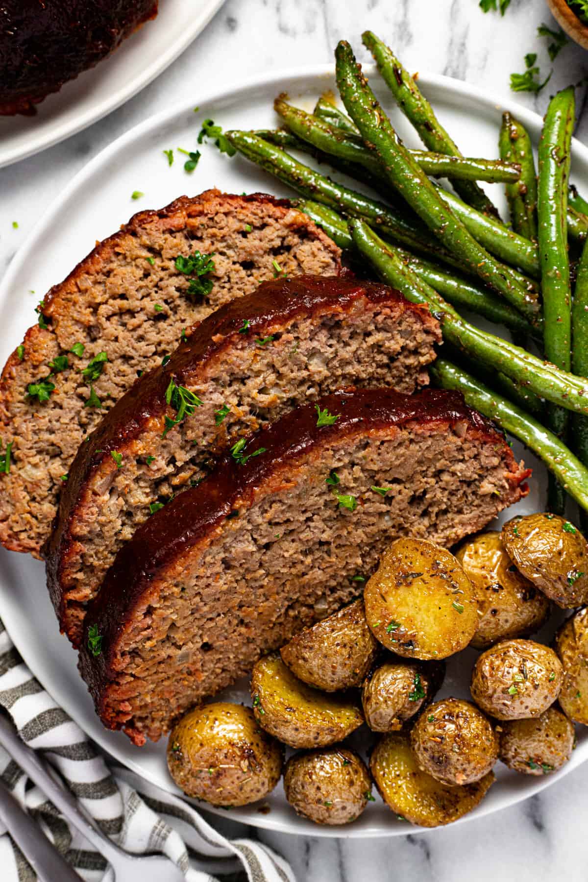 White plate with sliced meatloaf roasted potatoes and green beans.